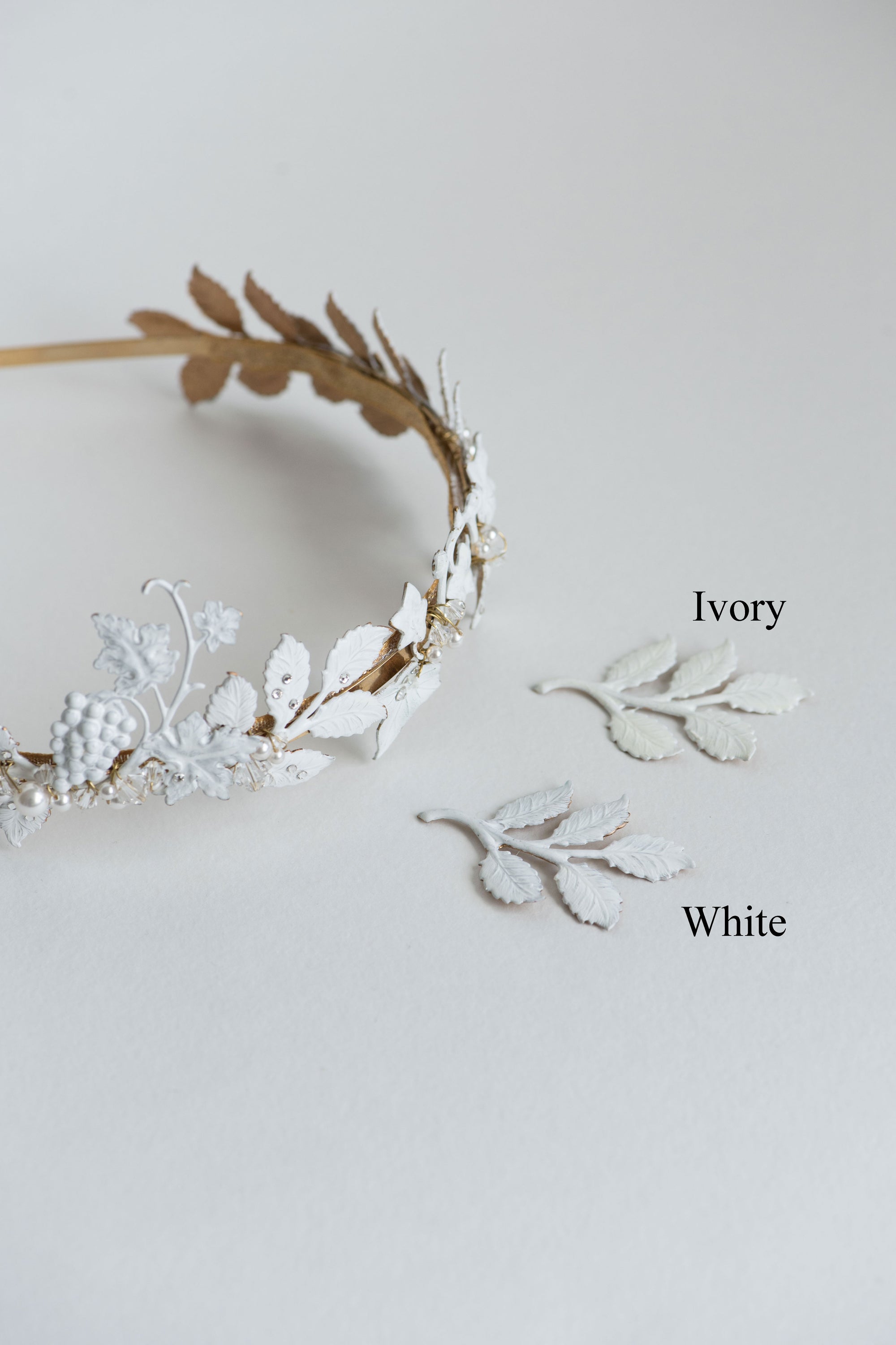 Side-by-side color comparison of VICTORIA bridal headband finishes: Hand-painted Matte White vs. Soft Ivory lacquer on gold brass leaves.