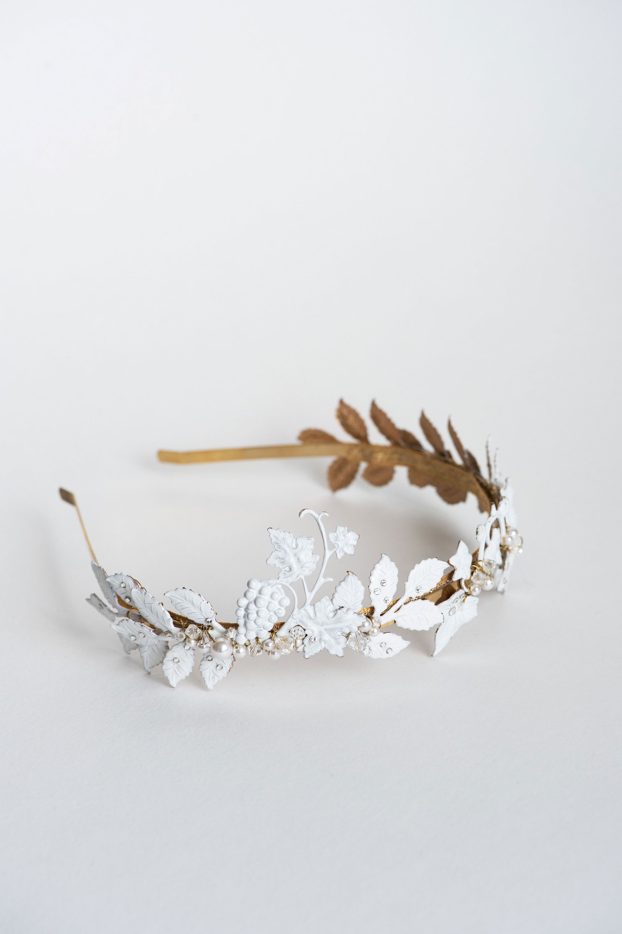 Detailed close-up of the VICTORIA bridal tiara featuring hand-painted white matte leaves, golden vine structure, and pearl accents with Austrian crystals, emphasizing the artisanal lacquer finish.