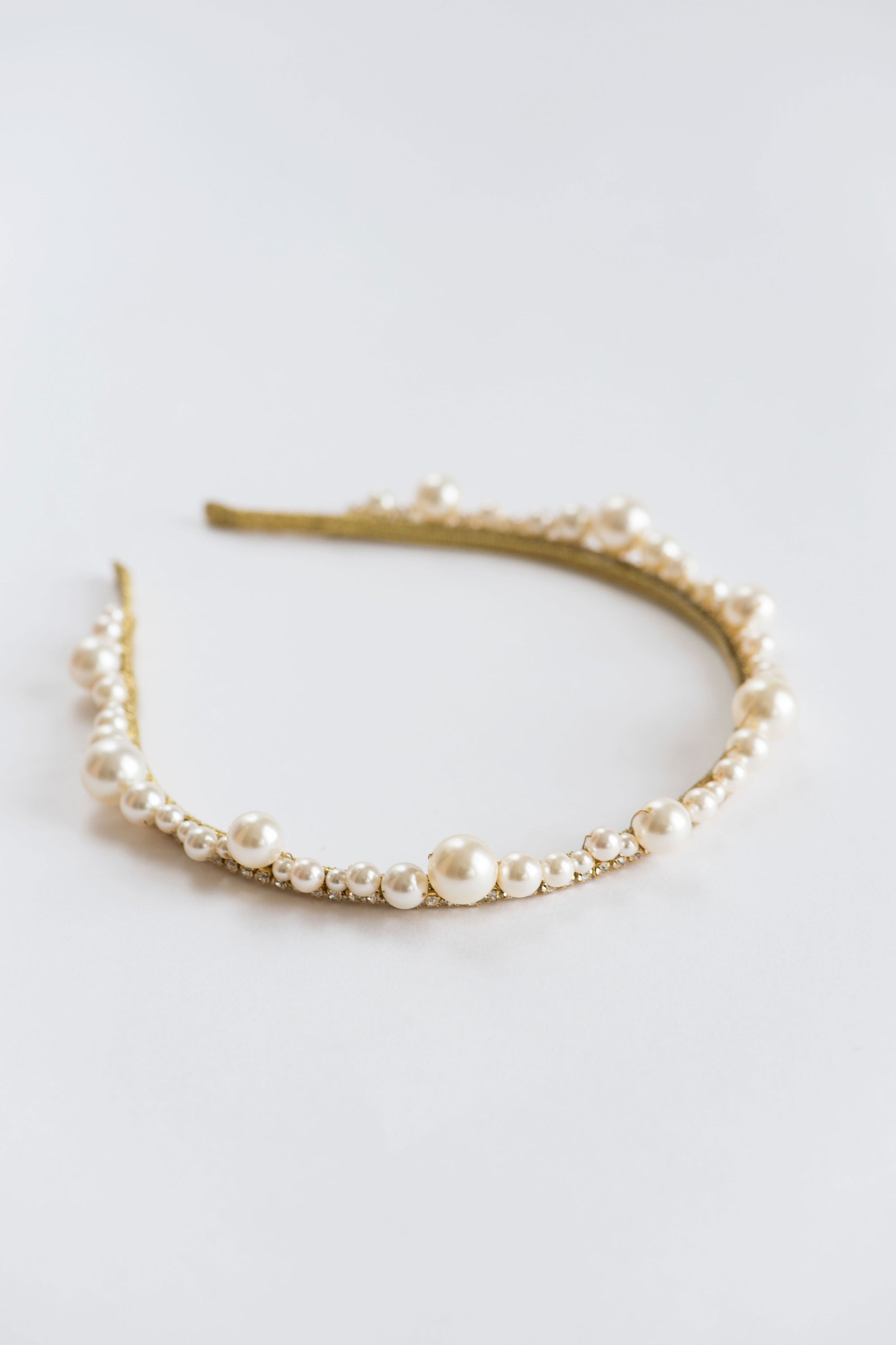 Close-up of handcrafted pearl bridal tiara showing scalloped rows of pearls and fine crystal accents on a metal headband