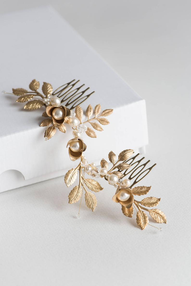 Overhead view of the TYCHE bridal hair vine comb on a white surface, showing the intricate arrangement of gold brass leaves, pearls, and two metal attachment combs in a botanical, Klimt-inspired layout.