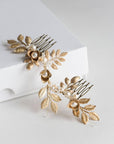 Overhead view of the TYCHE bridal hair vine comb on a white surface, showing the intricate arrangement of gold brass leaves, pearls, and two metal attachment combs in a botanical, Klimt-inspired layout.