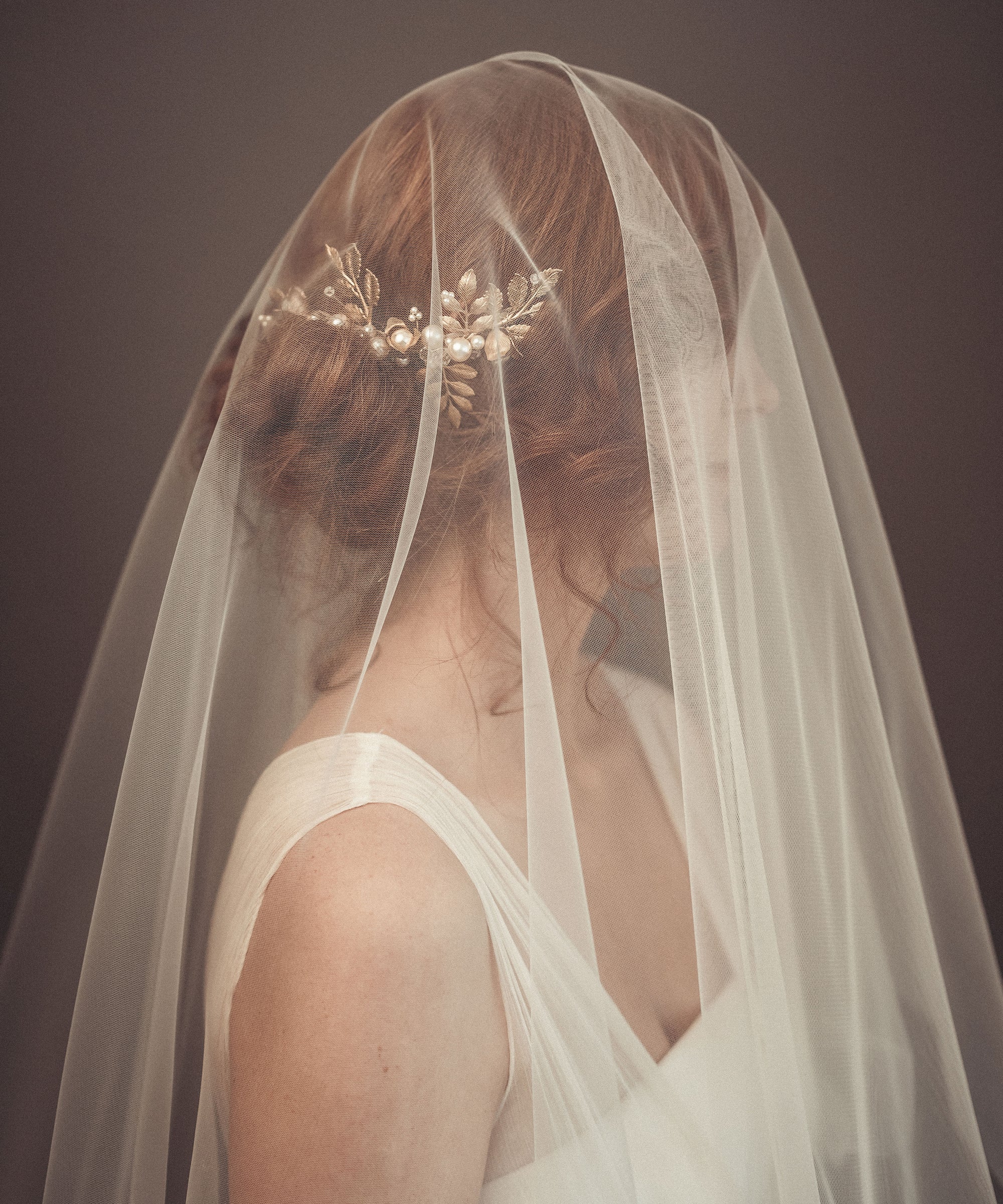 Fine art bridal portrait of a bride seen through a sheer tulle veil, wearing the TYCHE gold leaf hair vine comb for a romantic, ethereal wedding look.