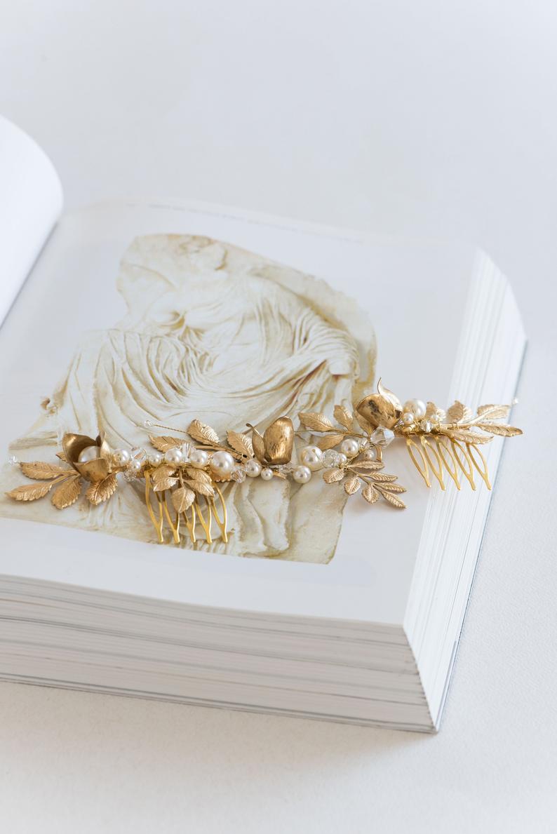 TYCHE bridal hair vine comb with gold brass leaves and pearls resting on an art book, showing the intricate sculptural floral design.
